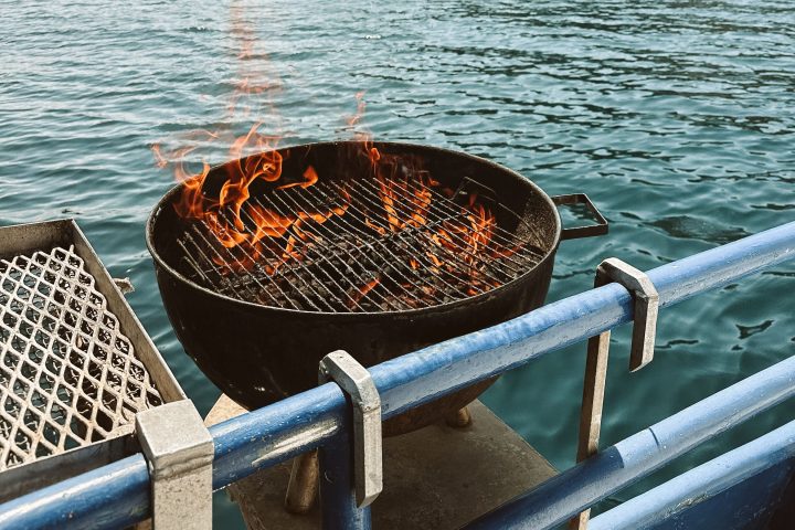 Burning grill on a boat with rocky island and lighthouse in the background.