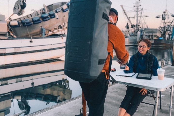 Person at table receives payment from another person near boats at a marina.