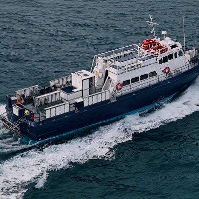 Blue and white boat sailing on a calm sea with a mountainous coastline in the distance.