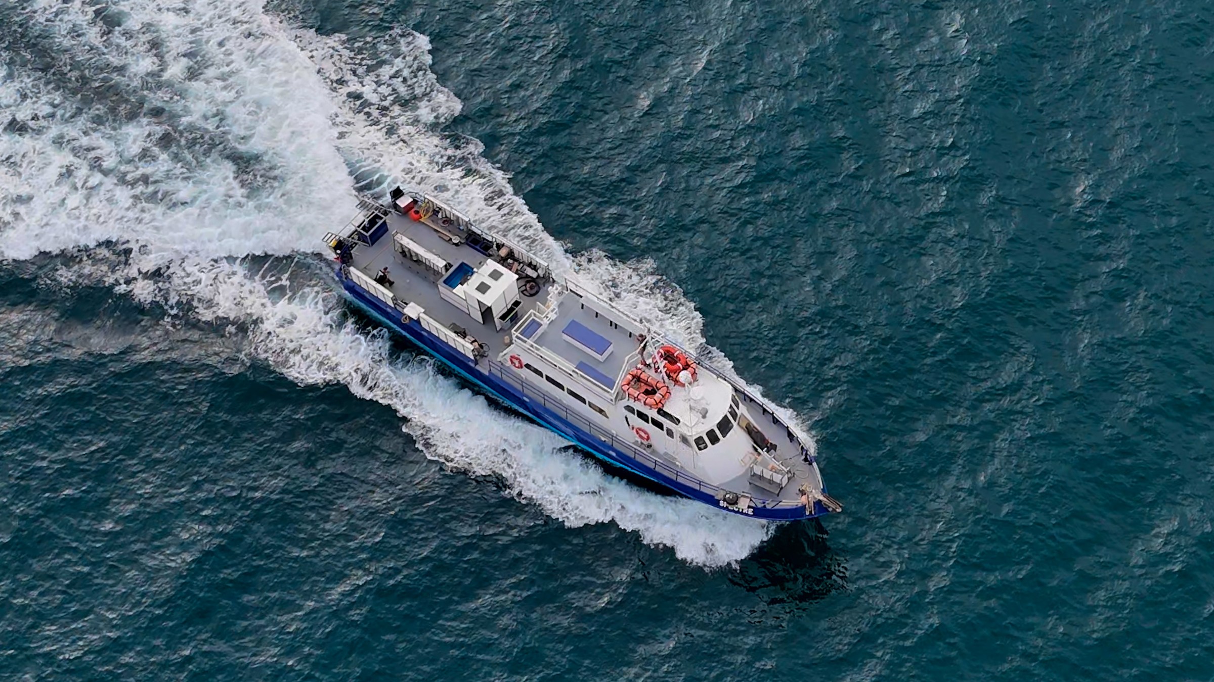 Aerial view of a white and blue boat navigating through waves on a vast body of water.
